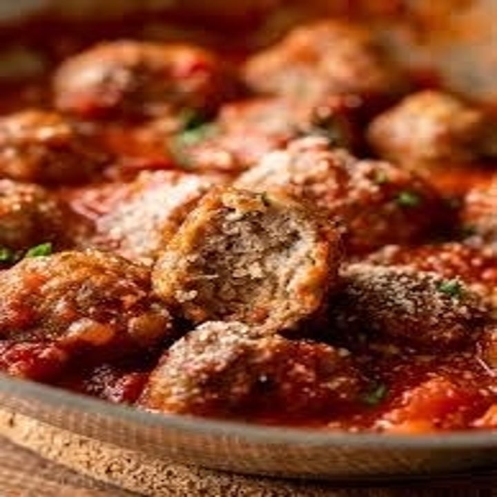 A bowl of cooked meatballs in tomato sauce with one sliced open to reveal a moist interior.