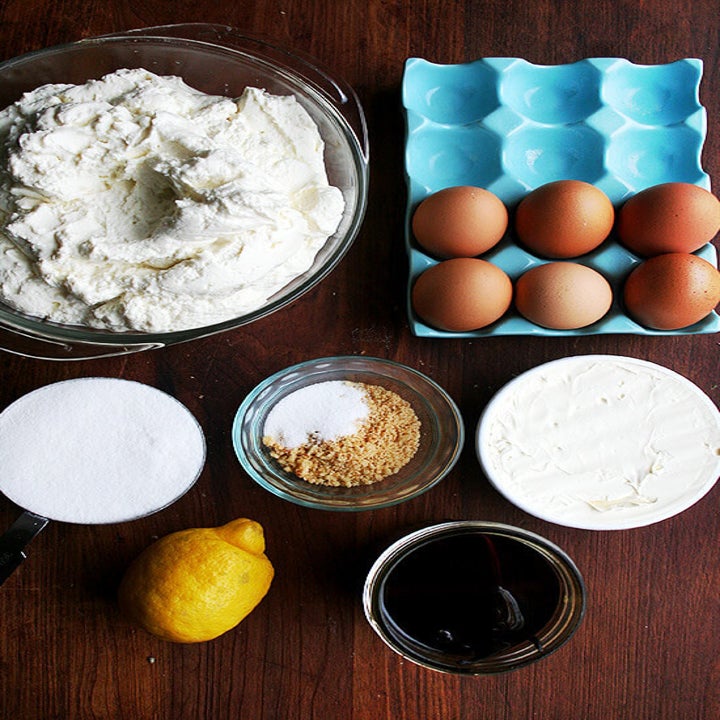 Ingredients for Italian cheesecake on a table including eggs, ricotta, lemon, sugar, and butter.