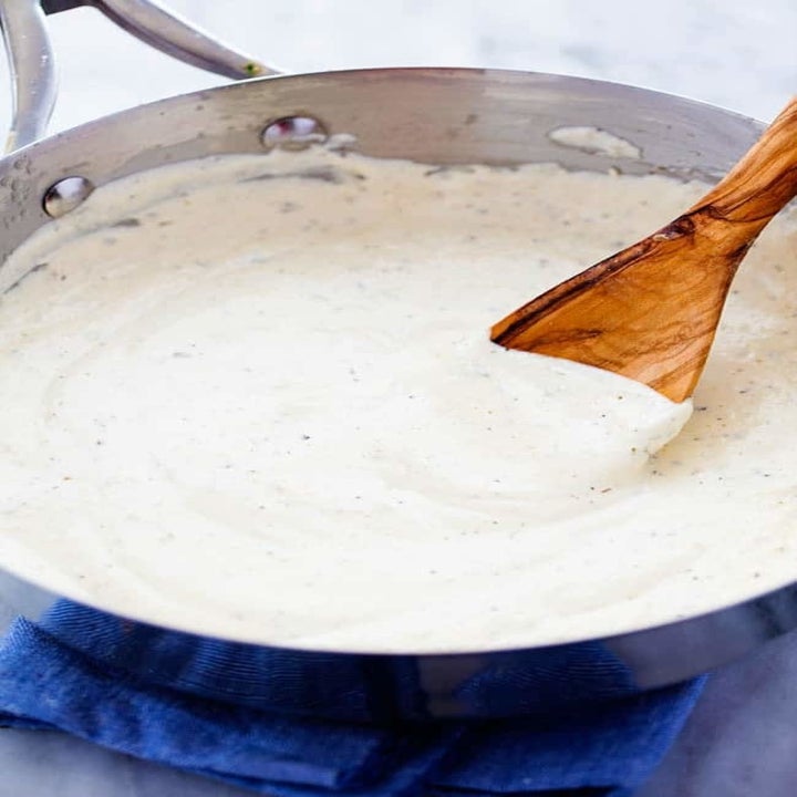 A wooden spoon stirring a pot of creamy alfredo sauce.
