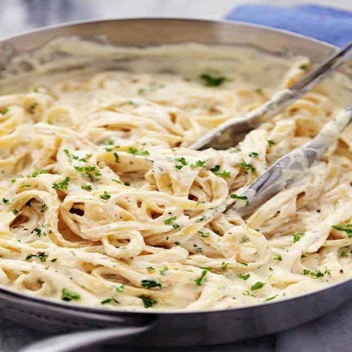 Tongs tossing fetuccine in homemade alfredo sauce.