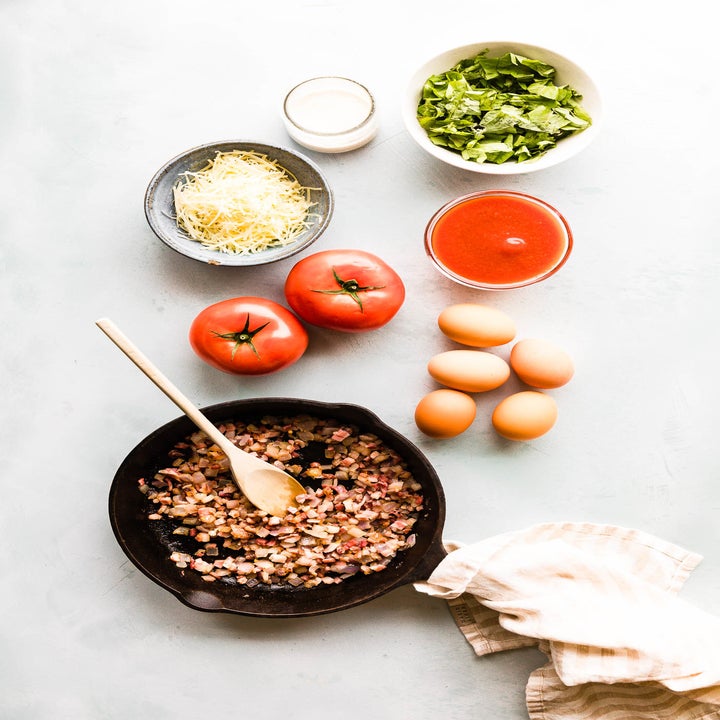 Ingredients for baked eggs including cheese, tomatoes, eggs, and diced pancetta.