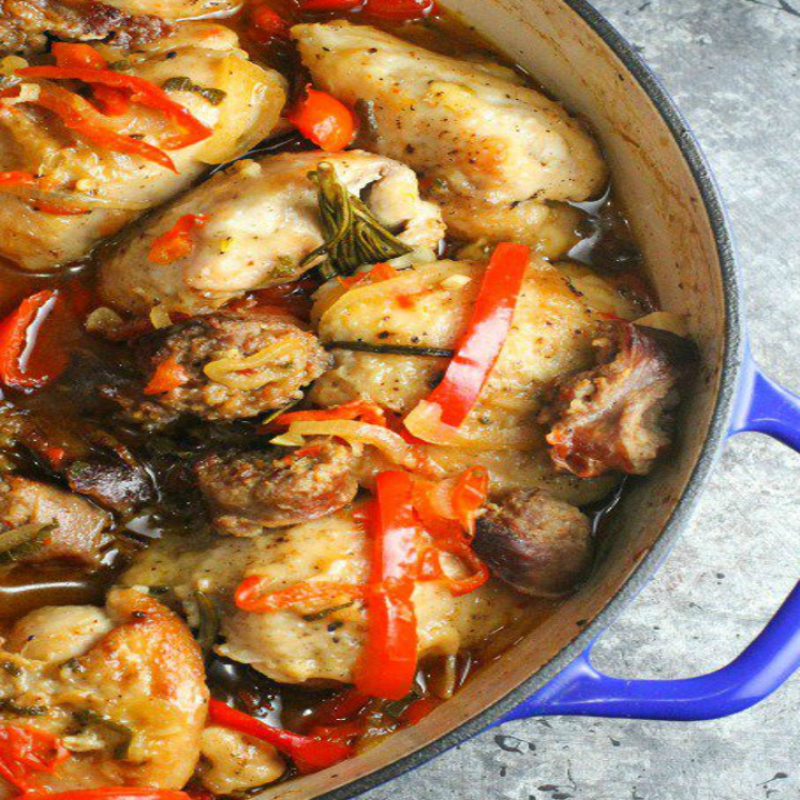A Dutch oven filled with chicken, hot sausage, and peppers.