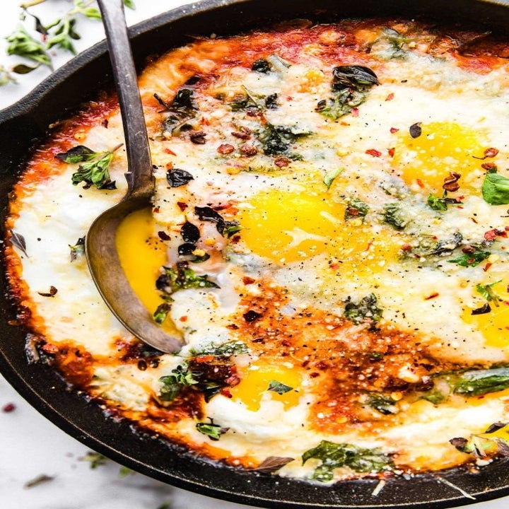 A spoon dunking into a skillet of baked eggs with a slightly runny yolk.