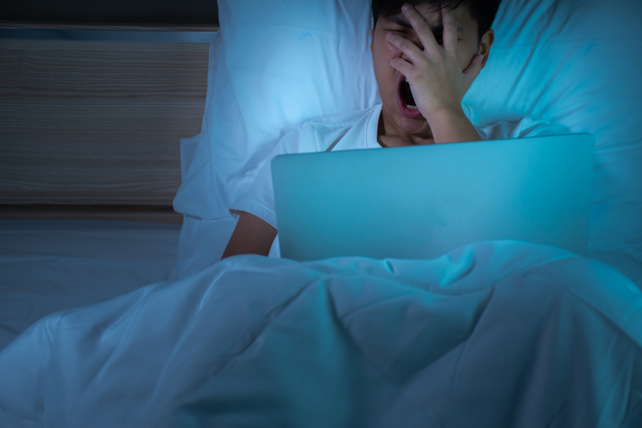 A person yawns while working on their bed