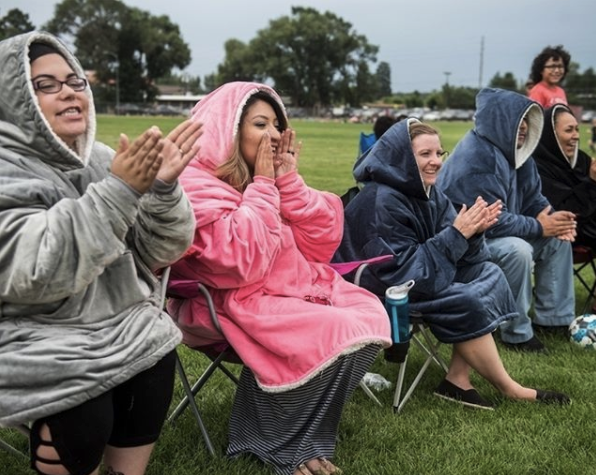 Five adults sit on foldable chairs outdoors, cheering presumably kids sports, off camera