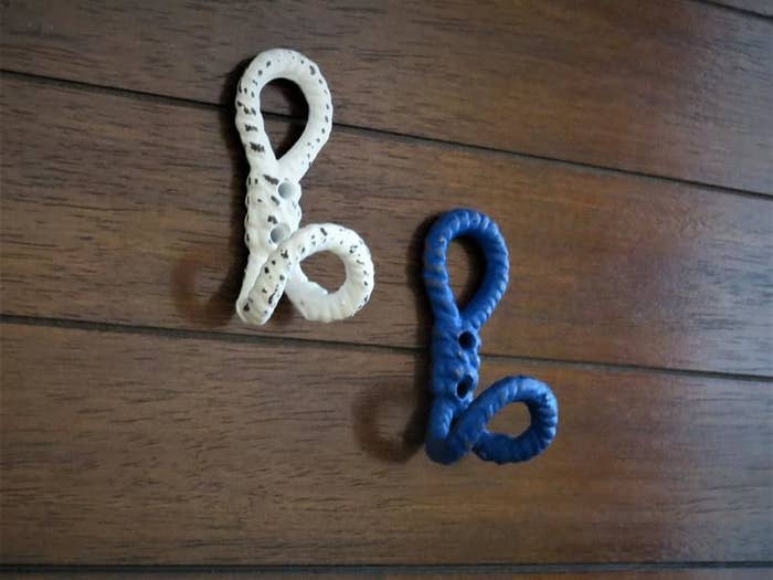 Two nautical knot hooks hang from a wall. One is white and the other is blue.