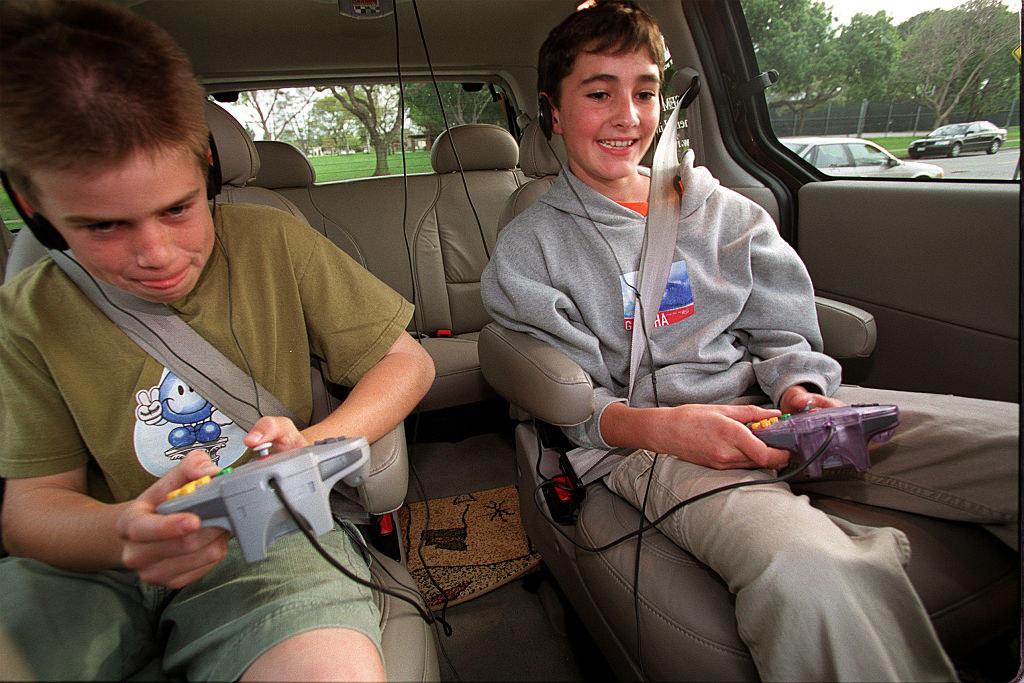 Two boys playing Nintendo 64 in the back of a car.