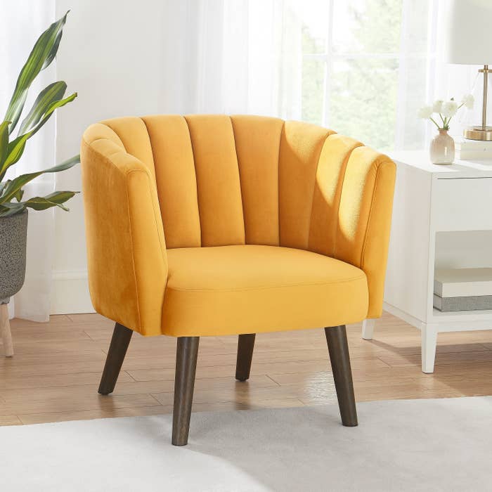 A mustard yellow chair with full back and arms and brown wooden legs