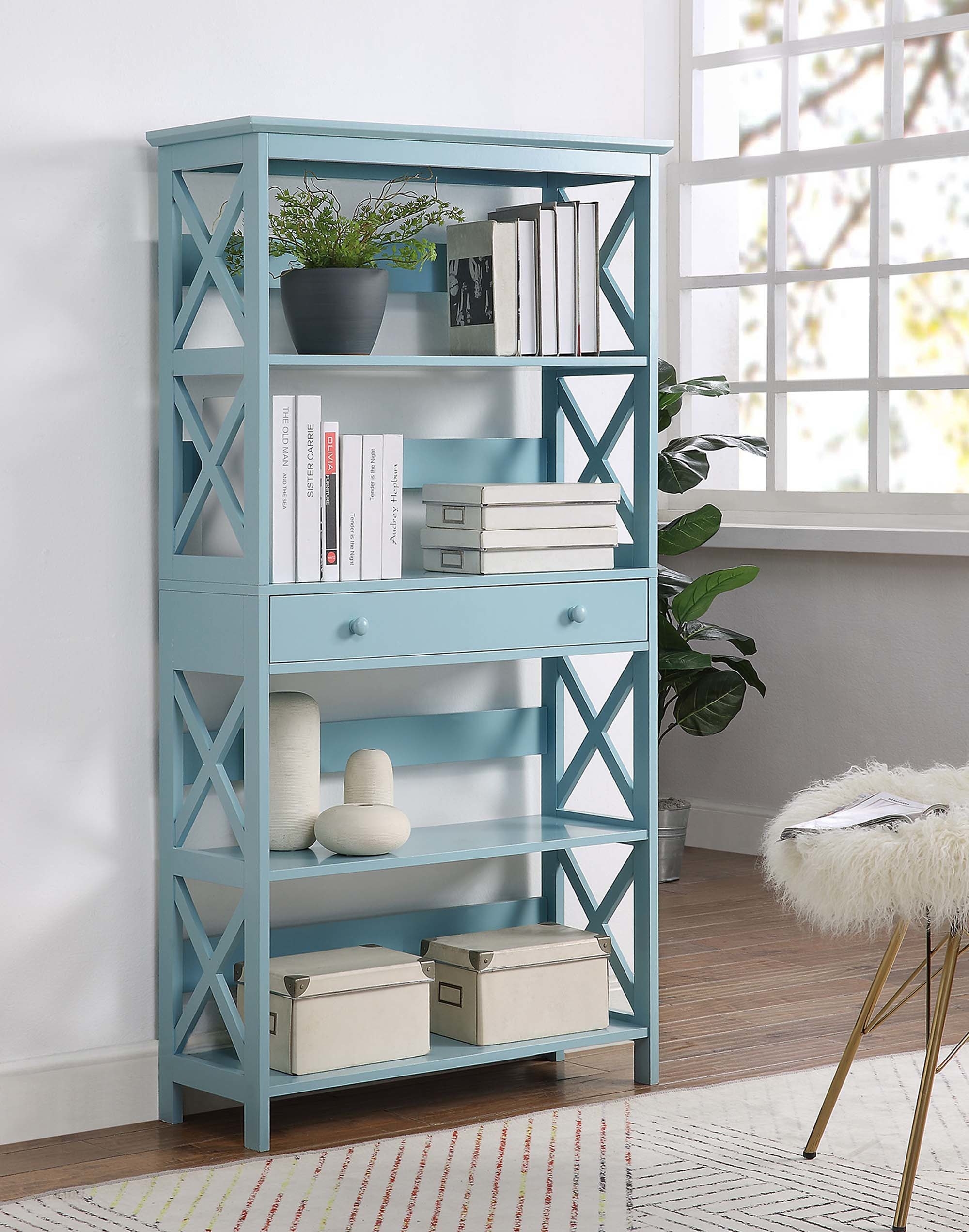 A sea-foam colored bookshelf with a drawer in the middle separating two shelves on the bottom and two on the top