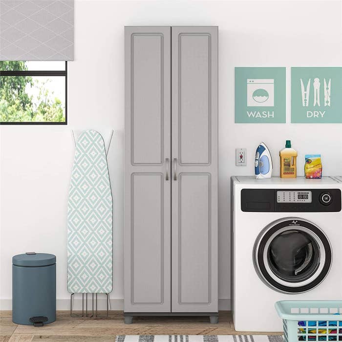 A tall and thin cabinet with two doors in grey in a laundry room