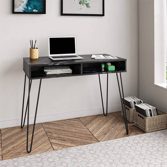 A simple black desk with two open storage shelves and wire legs