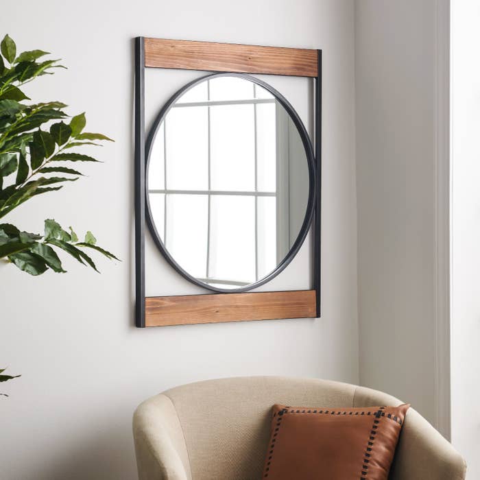 A circular mirror with a black metal frame situated between two horizontal pieces of wood and two vertical metal frames