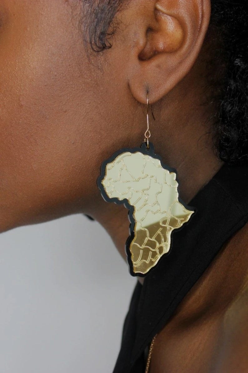 A person wears an earring in the shape of Africa