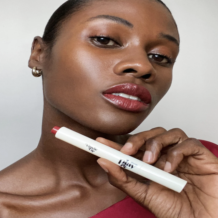 a model holding up the vinylic lipstick with a soft red lip on