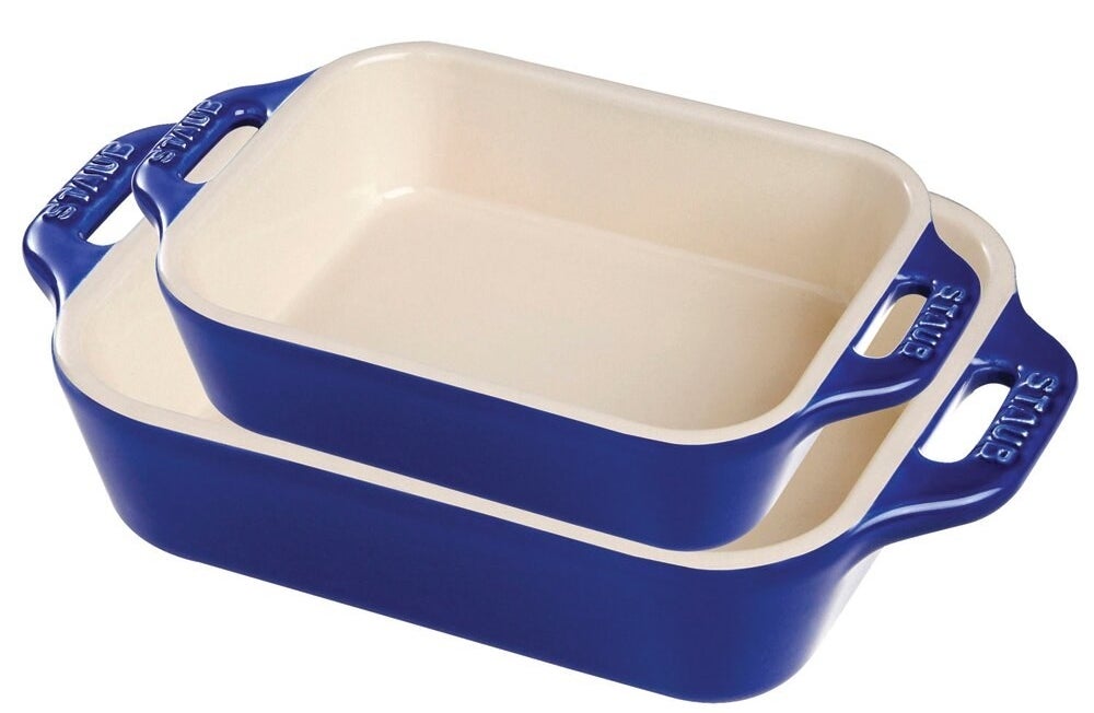 Two Staub baking dishes with blue exteriors, white interiors, and handles on the side