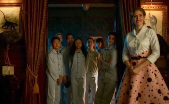 The young versions of the Umbrella Academy standing in a doorway wearing pyjamas, accompanied by Grace