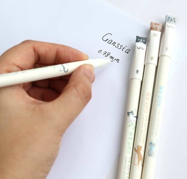 model writing on paper with black ink next to white pens with cat-inspired tips