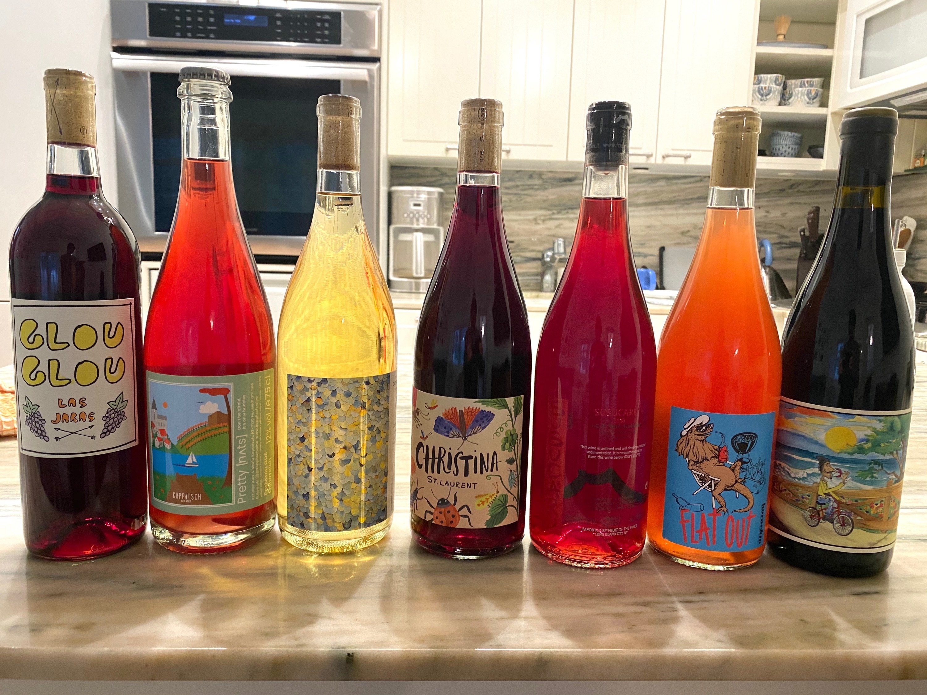 A handful of natural wines on a countertop containing some reds, rosés, and white wines.