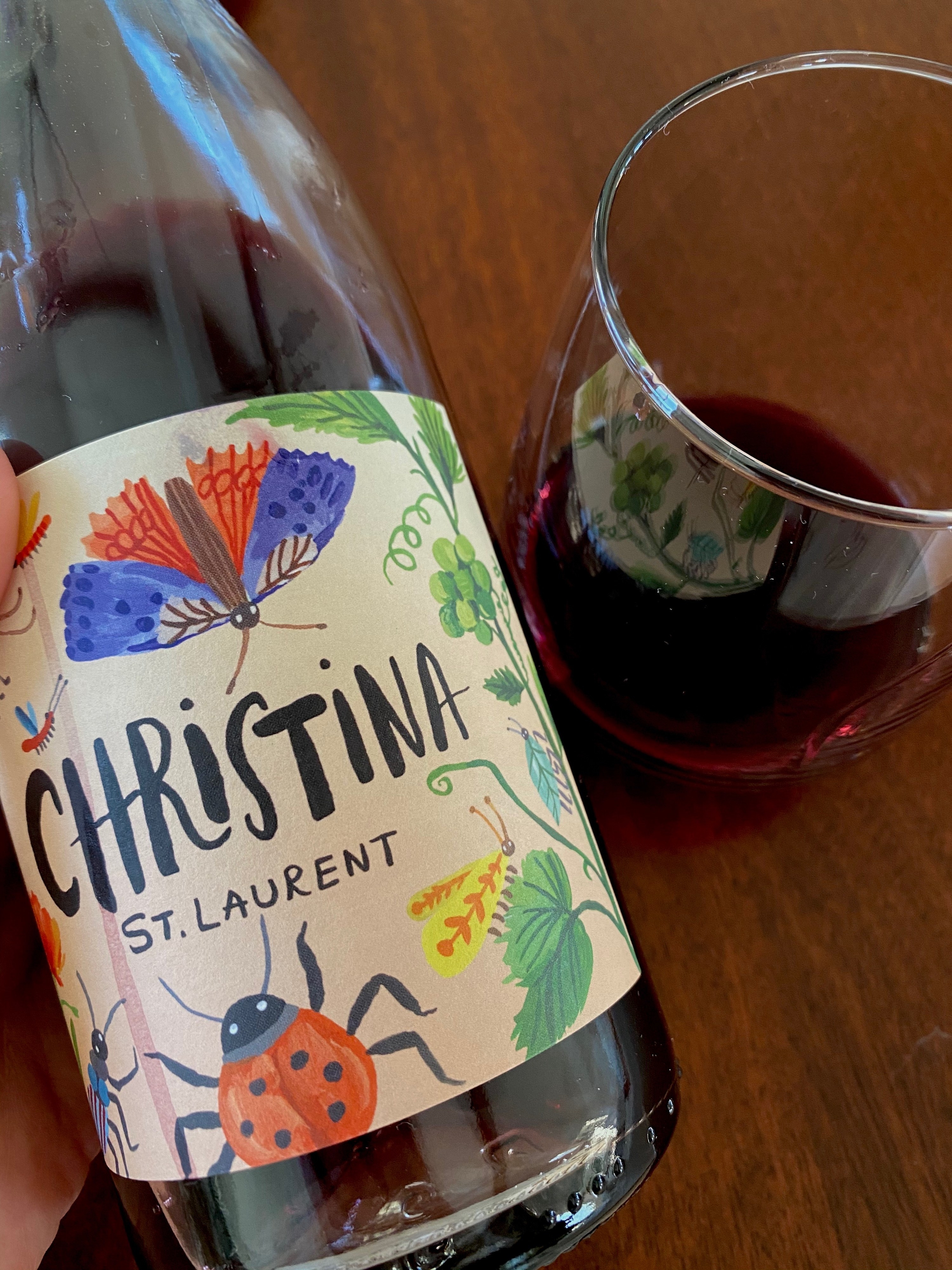 A bottle of red wine with a cute label with a ladybug and butterfly.