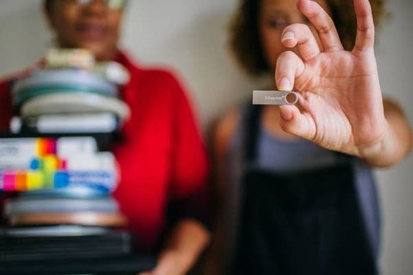 In-focus shot of person holding a flash drive next to another person holding a stack of videos