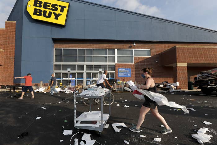 People clean up scattered debris and trash in a parking lot outside of a Best Buy store.