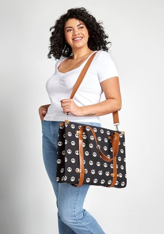 A model carrying the black and white tote with brown straps by the shoulder strap
