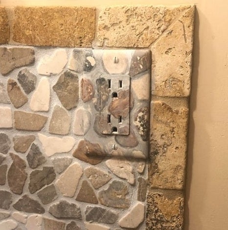 A wall outlet painted with rock designs that match the pattern on the wall