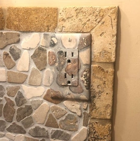 A wall outlet painted with rock designs that match the pattern on the wall