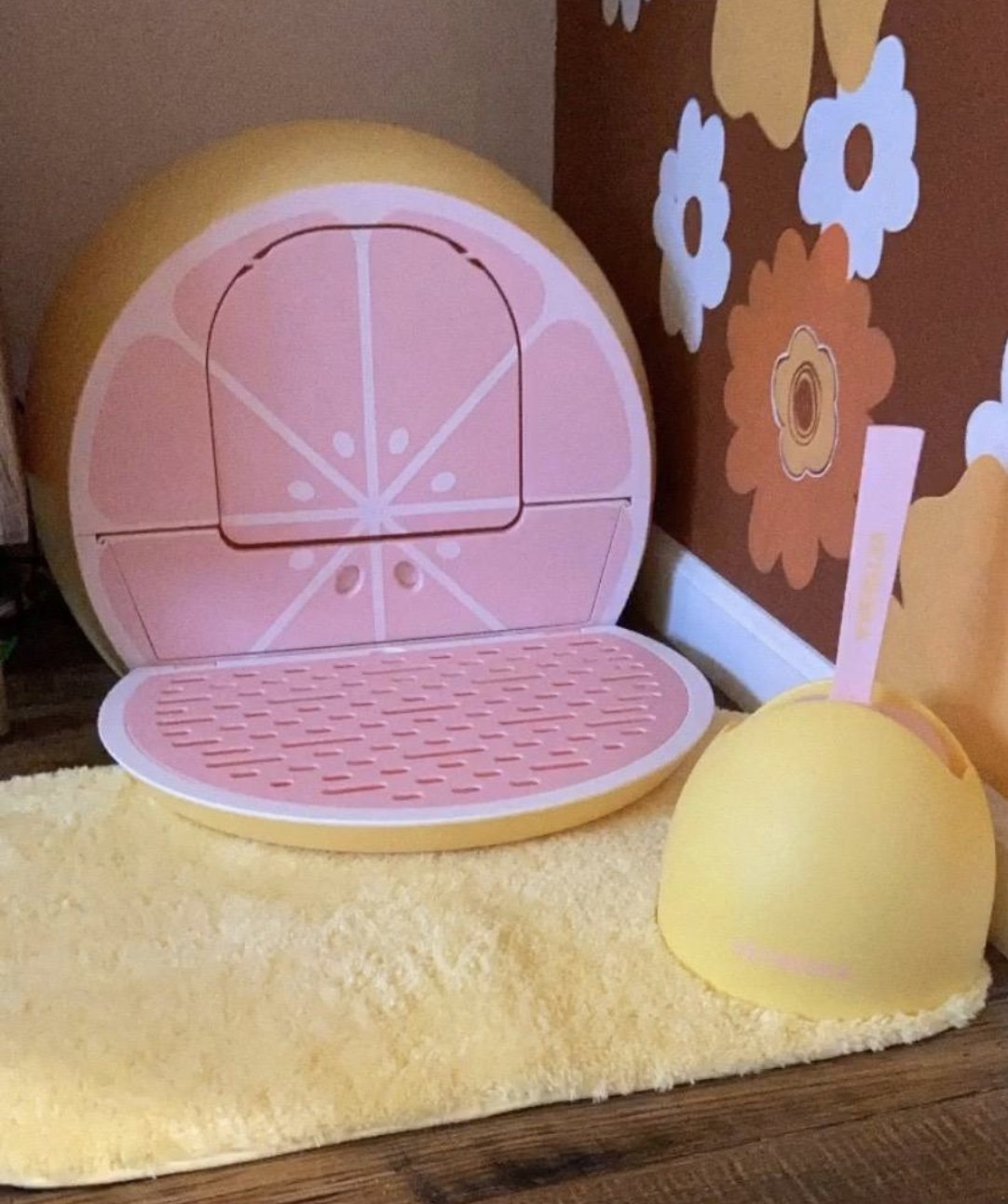 An image of a litter box shaped like a grapefruit. There is a catch tray in front of the opening and a swinging door to enter the box. There is a matching scooper. 