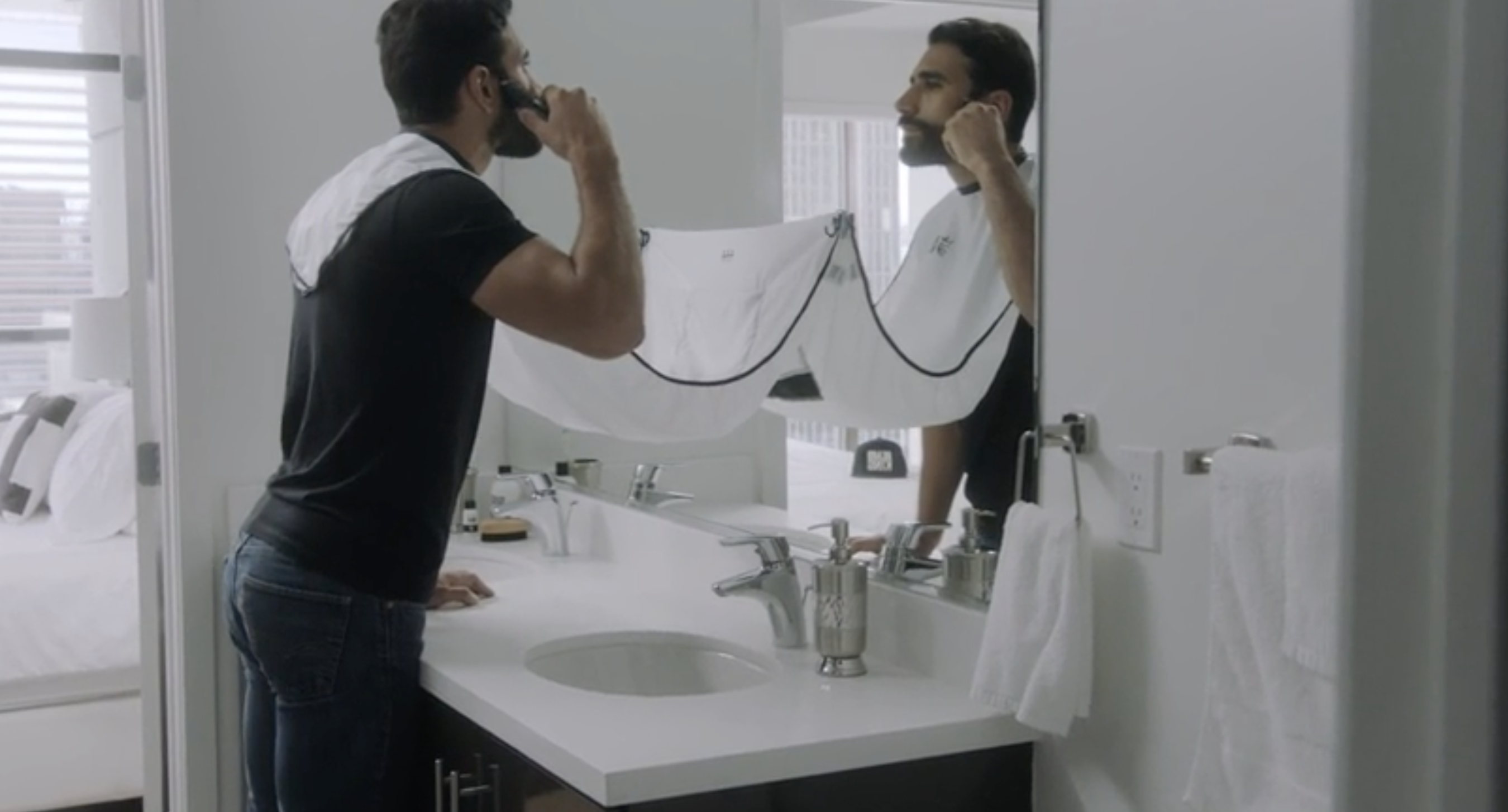 A model trimming their beard over a plastic &quot;bib&quot; that is attached to their neck and suctioned to the bathroom mirror