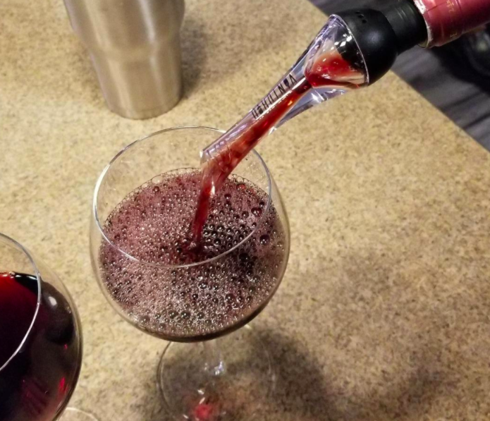 A reviewer pouring wine into a glass using the aerator — there are bubbles at the top of the glass from it being aerated 