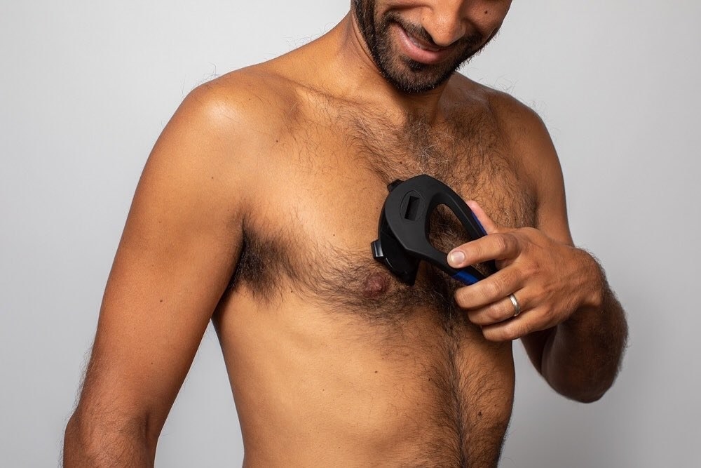 A smiling person using the shaver to trim their chest hair