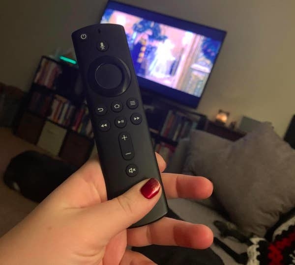 A reviewer holding their Fire TV Stick while watching TV