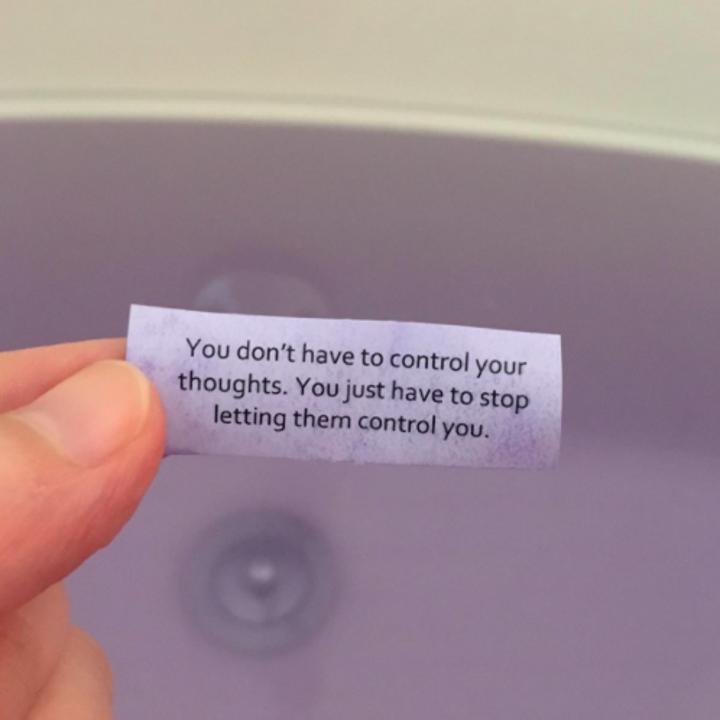 A person holding one of the messages that comes inside the bath bomb that reads "you don't have to control your thoughts, you just have to stop letting them control you"