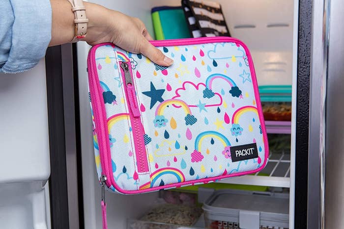 A model&#x27;s hand placing a bright pink trimmed lunch bag with rainbow designs into a fridge