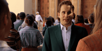 A gif from The Politician showing Payton fist pumping two characters partially off screen in a school yard wearing a green jacket and white shirt on a sunny day