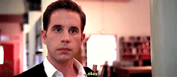 A gif from The Politician showing a close up of character Payton in a library wearing a white shirt and a black sweater and saying okay in an uncertain way