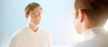 A gif from The Politician showing River and Payton in a dreamy landscape both wearing white sweaters and walking towards each other for a hug