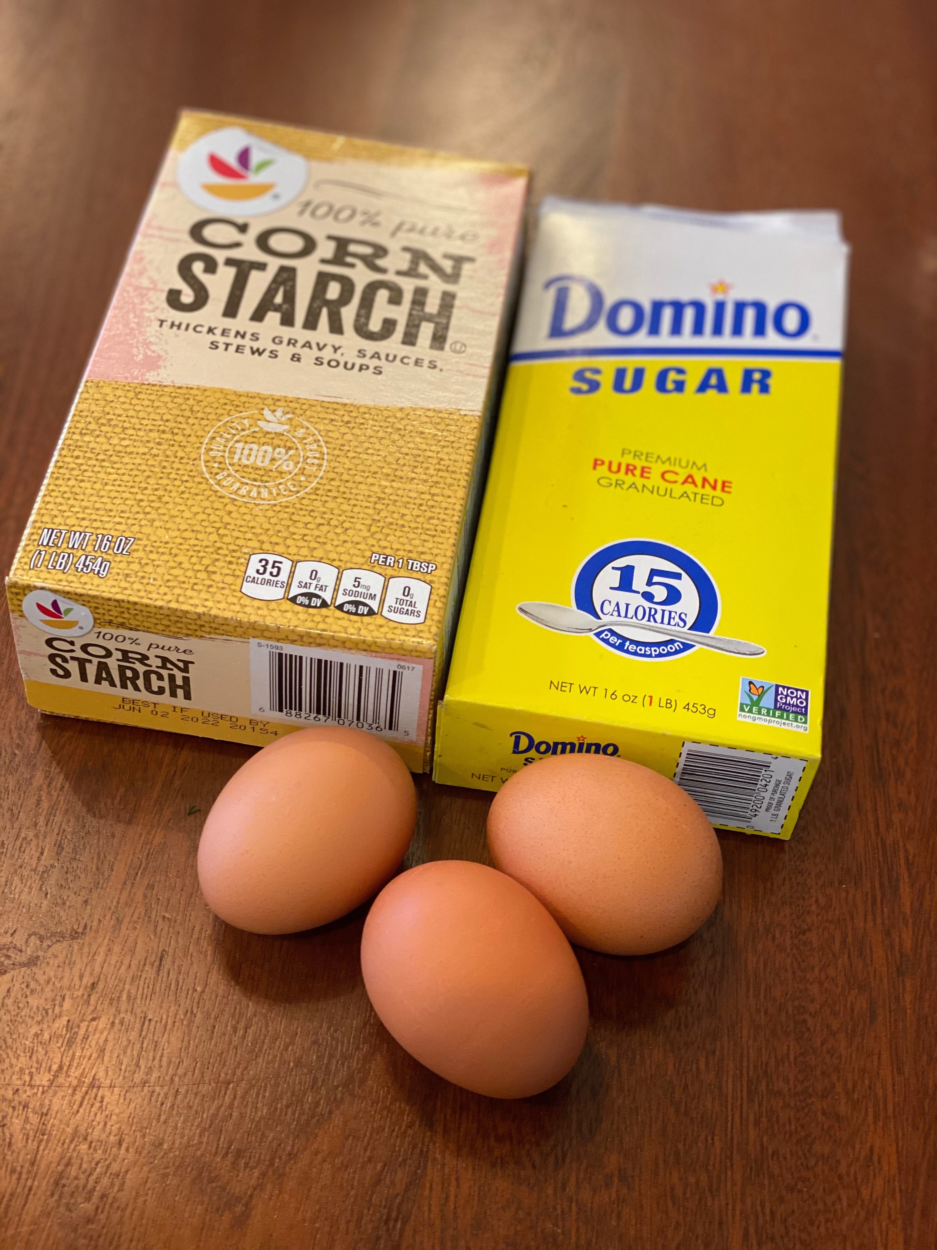 Three eggs, sugar, and cornstarch on a wooden countertop for cloud bread.