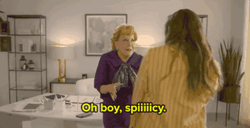 A gif from The Politician showing Bette Midler as her character Haddasah in her clean white office addressing macafee who is in front of the camera. Haddasah wears a purple suit and shakes her body and hands while saying oh boy spicy