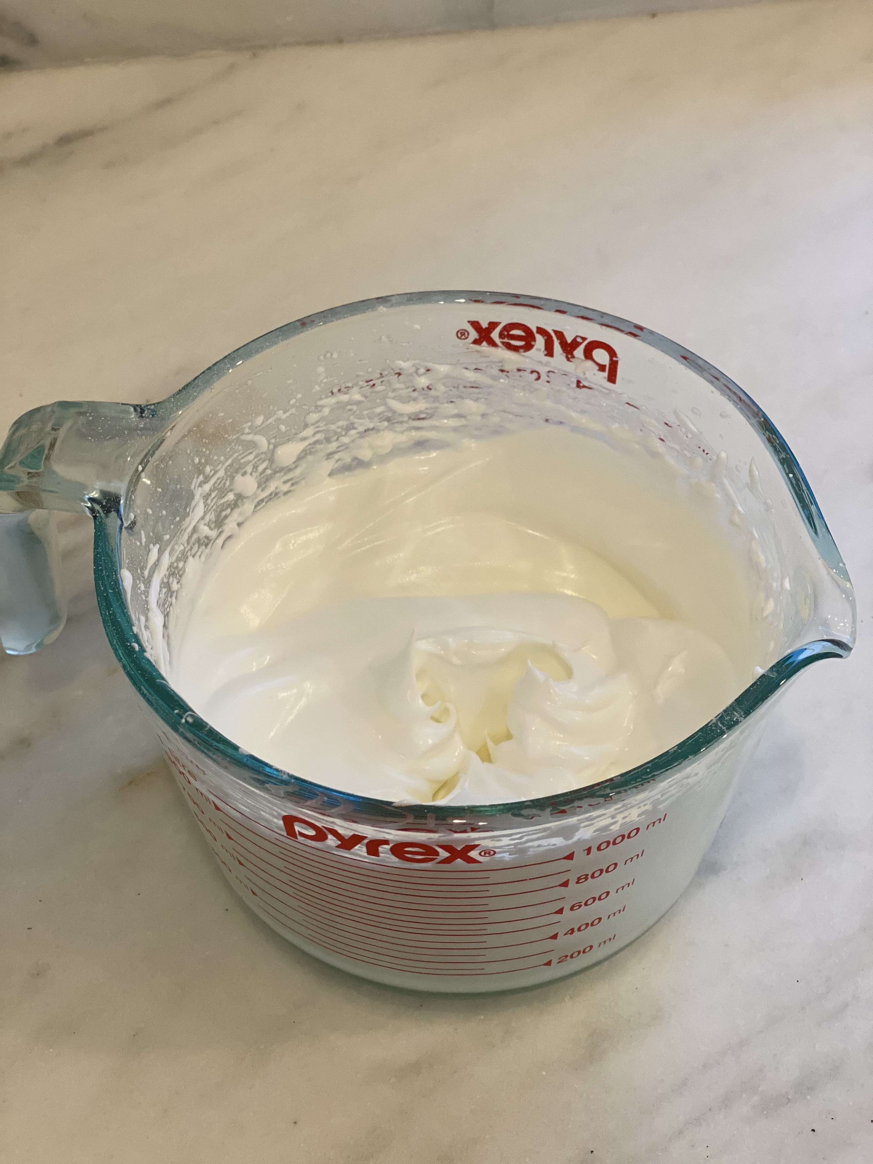 The egg white mixture with stiff peaks in a measuring cup.