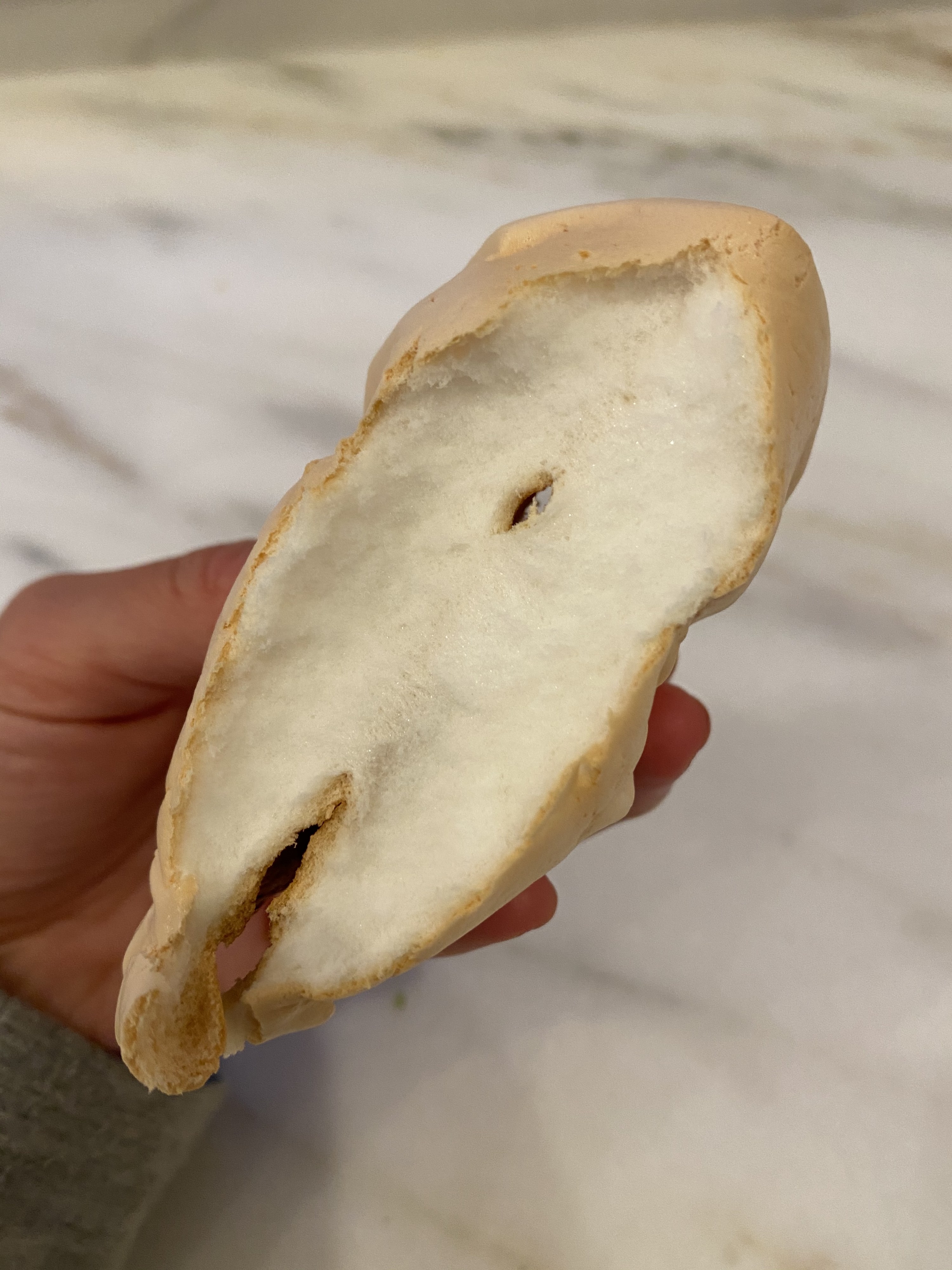 My hands holding a piece of cloud bread that is split in half, revealing a white and fluffy interior.