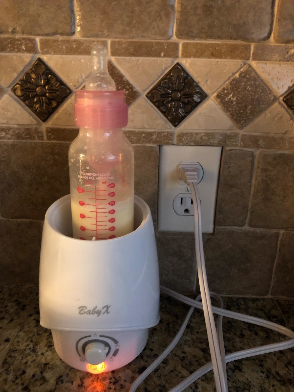 A reviewer&#x27;s image of a white bottle warmer with a milk bottle being warmed