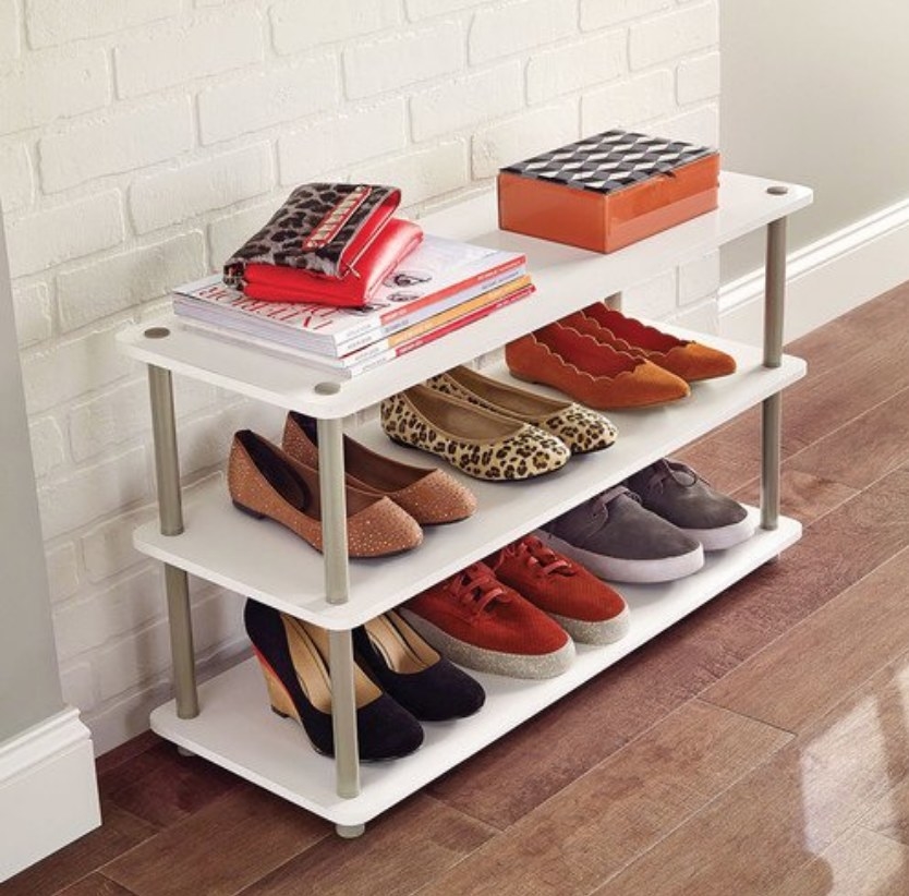 Three white shelves holding various shoes and books