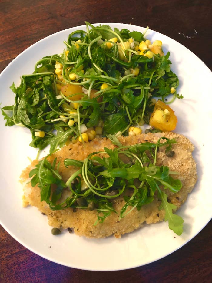 A plate with breaded fish Milanese and arugula salad.