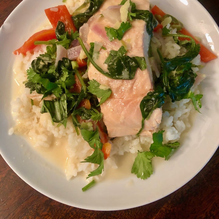 A bowl of salmon coconut curry with spinach, peppers, and rice.
