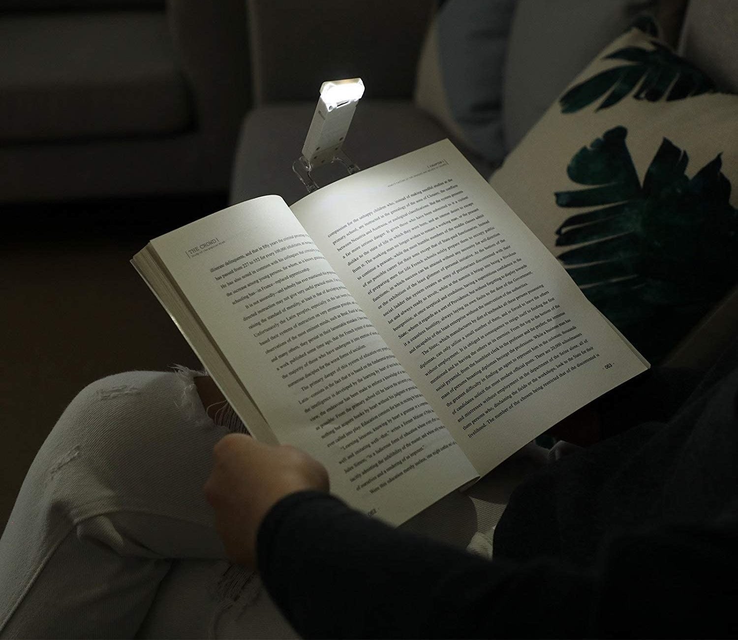 A person reading a large book in the dark There is a small book light attached to the top of the book