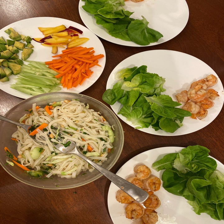 Four plates with lettuce, shrimp, sliced vegetables, and a big bowl of noodle salad.