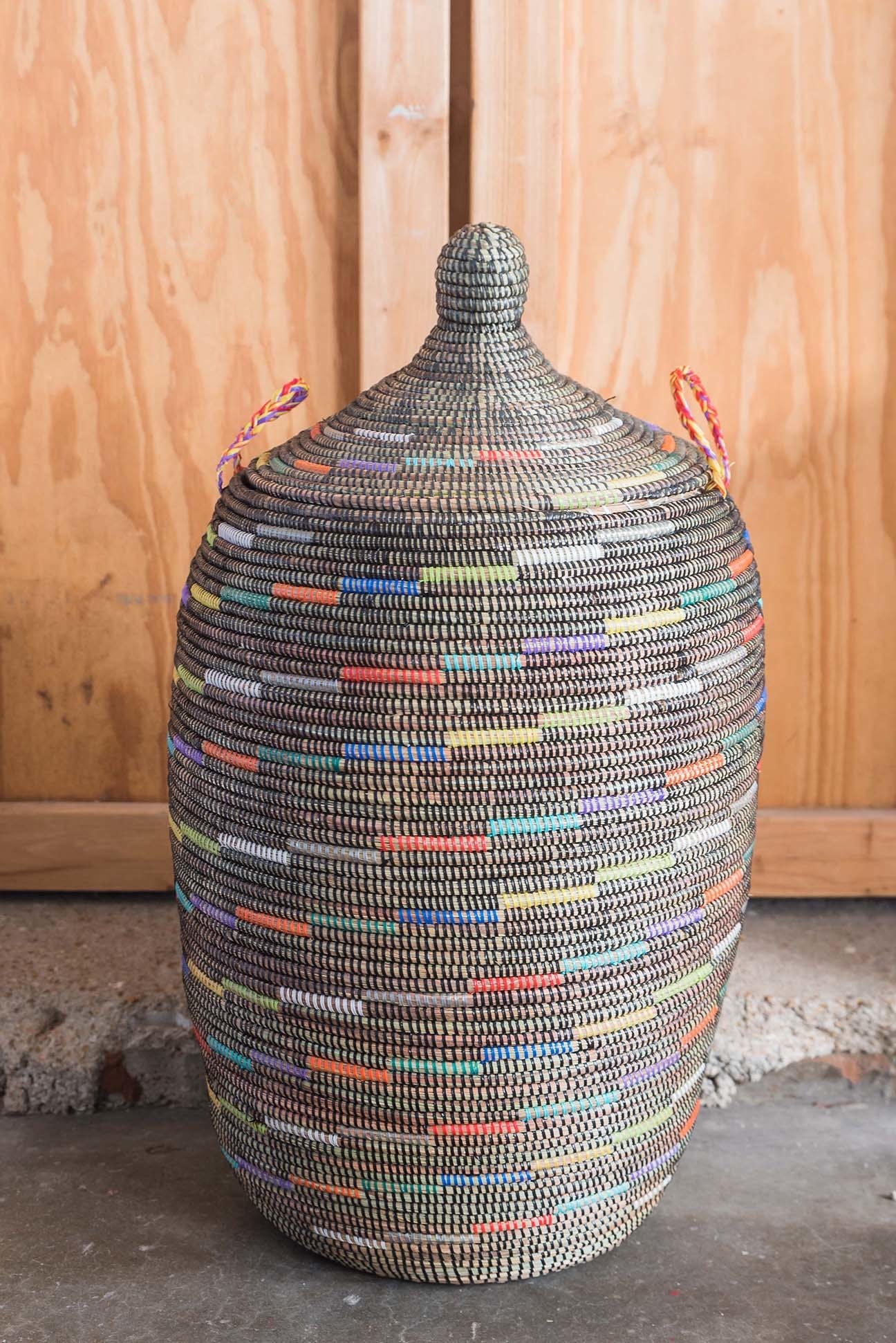 A large woven basket with a lid and handles on the side with black and multi-colored lines all over