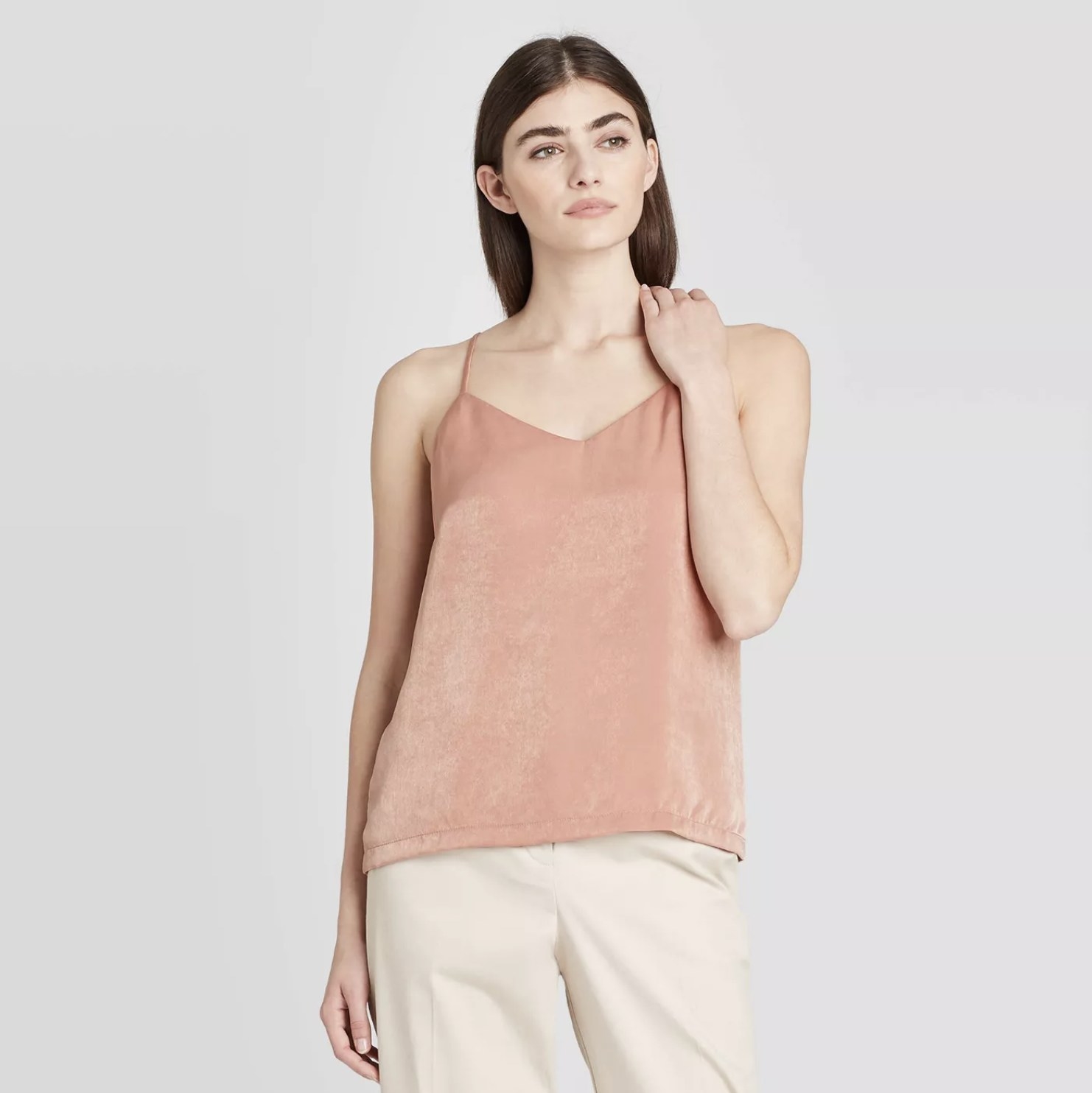 Model is wearing a blush pink v-neck tank top and cream slacks